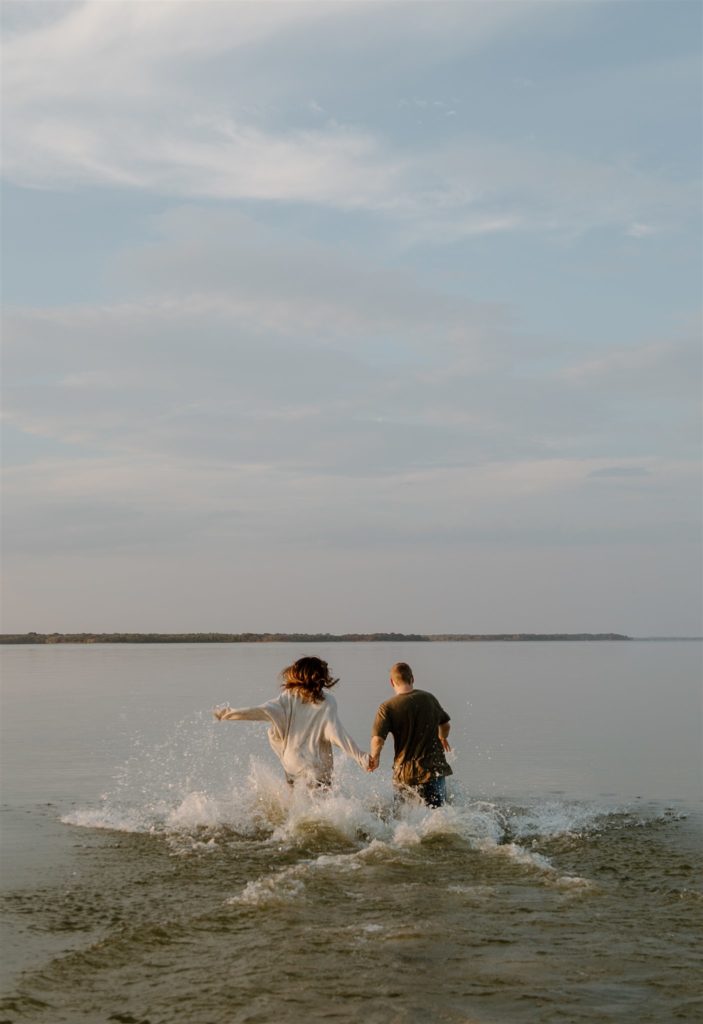 Couple running into Lake Tawakni during engagement photos during golden hour.