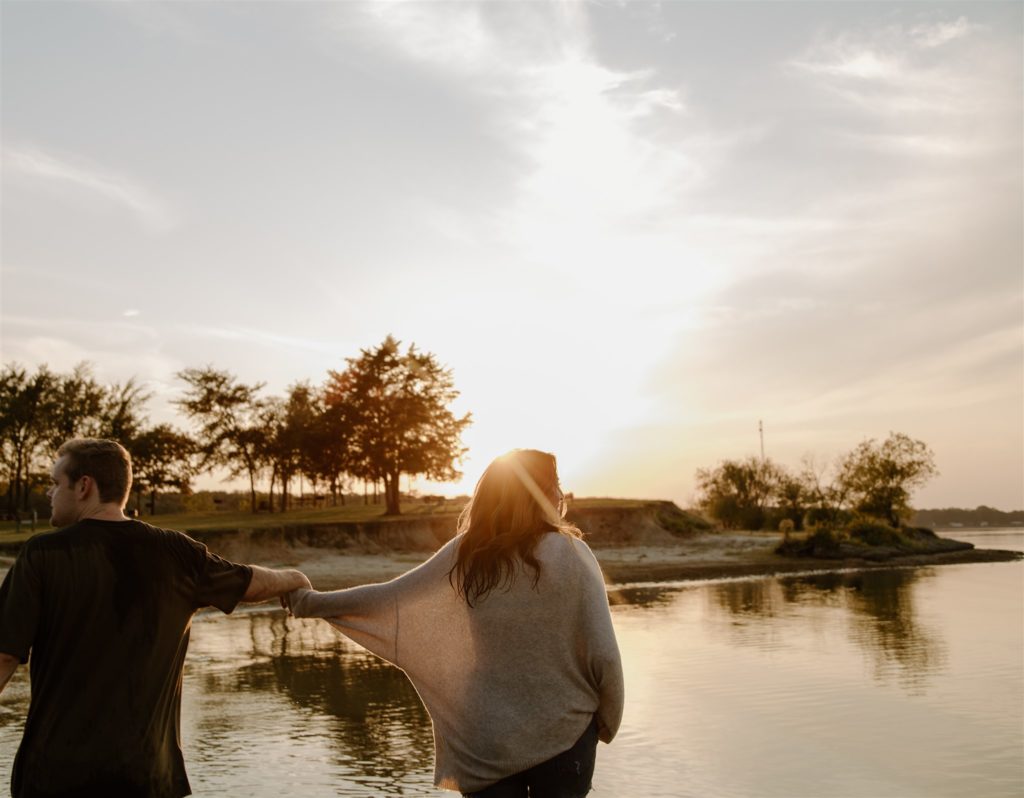 Couple walking and holding hands on beach at Lake Tawakoni during golden hour.