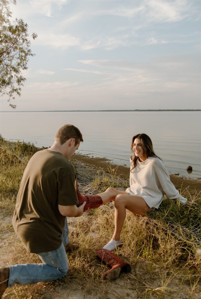 Couple taking shoes off during lakeside engagement photos.