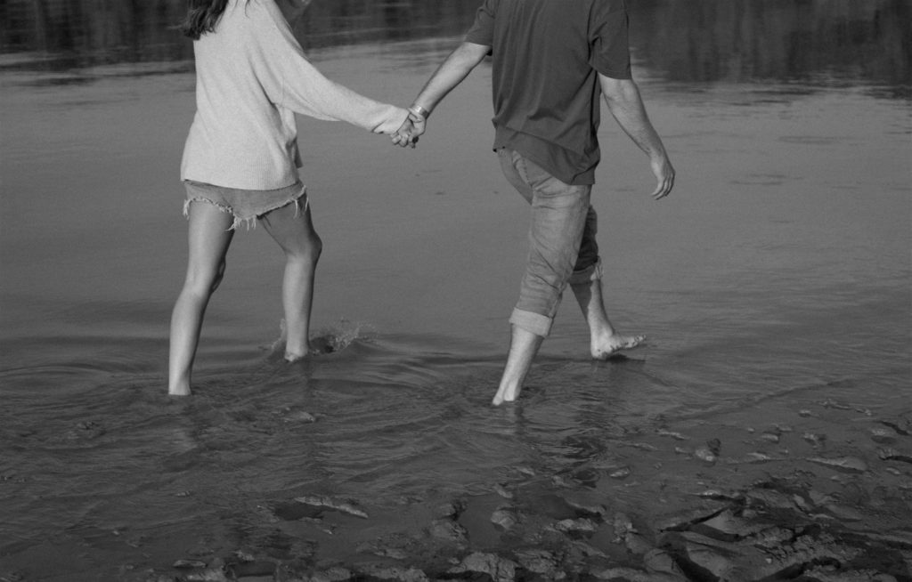 Couple walking in lake during engagement photos in black and white.