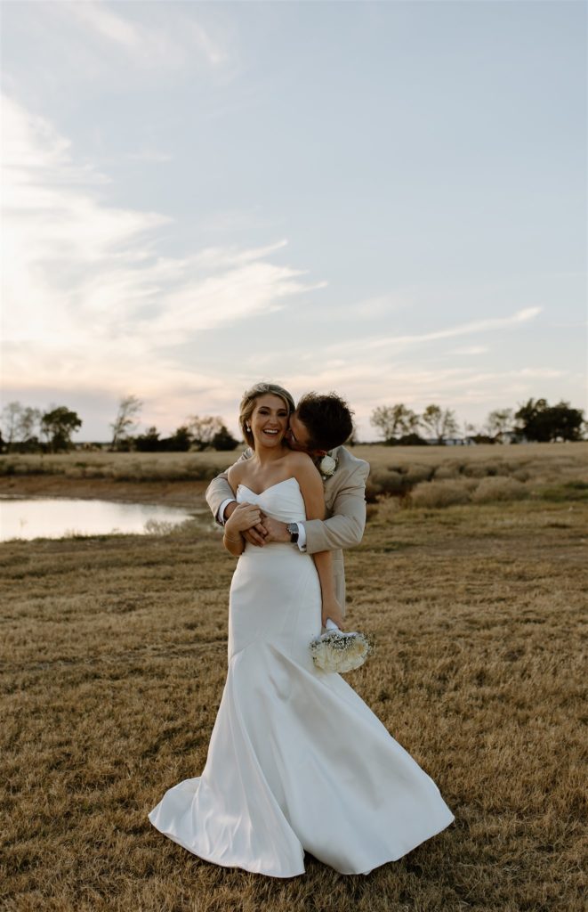 Groom kisses bride's neck during golden hour after texas wedding ceremony.