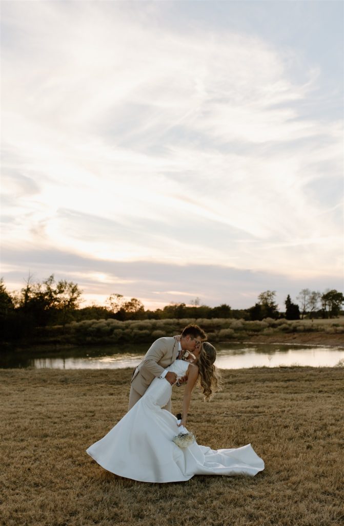 Bride and groom dip kiss in front of lake at texas wedding venue. 