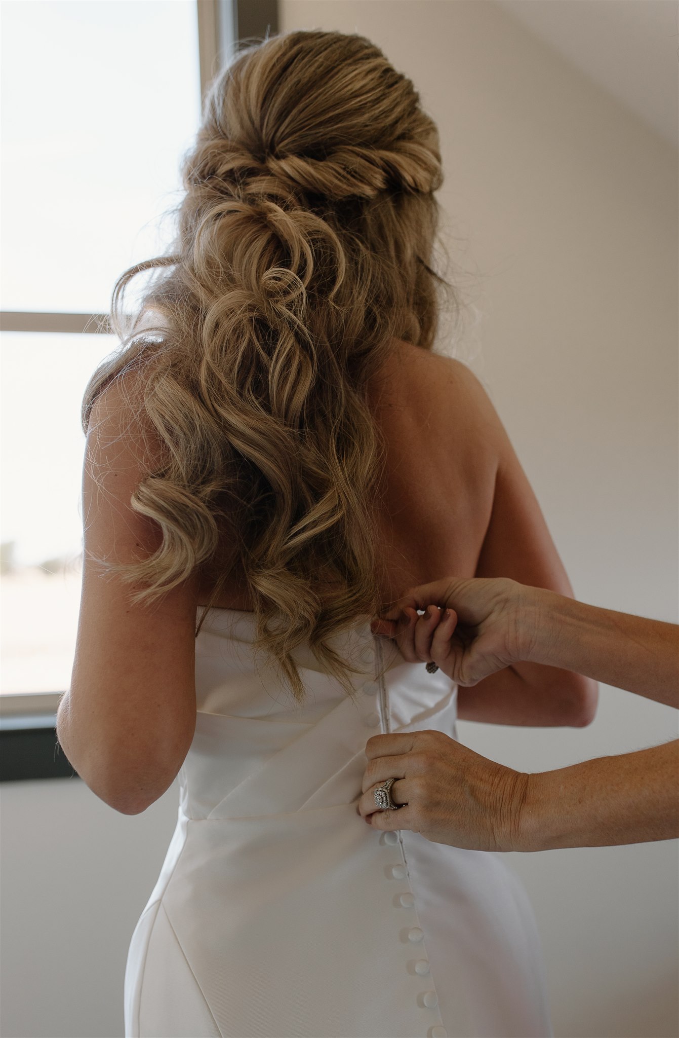 Mother of bride zips bride's dress while getting ready.