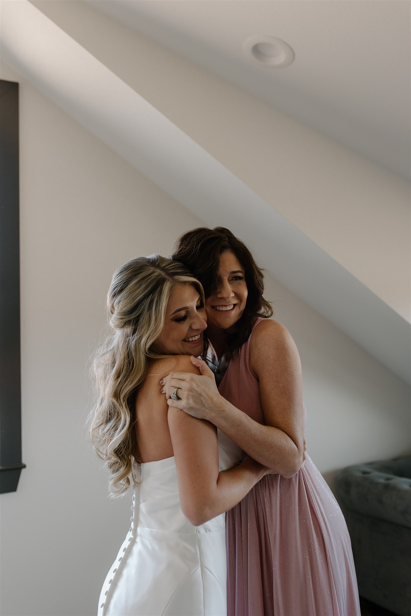 Mother of bride and bride embrace while getting ready.