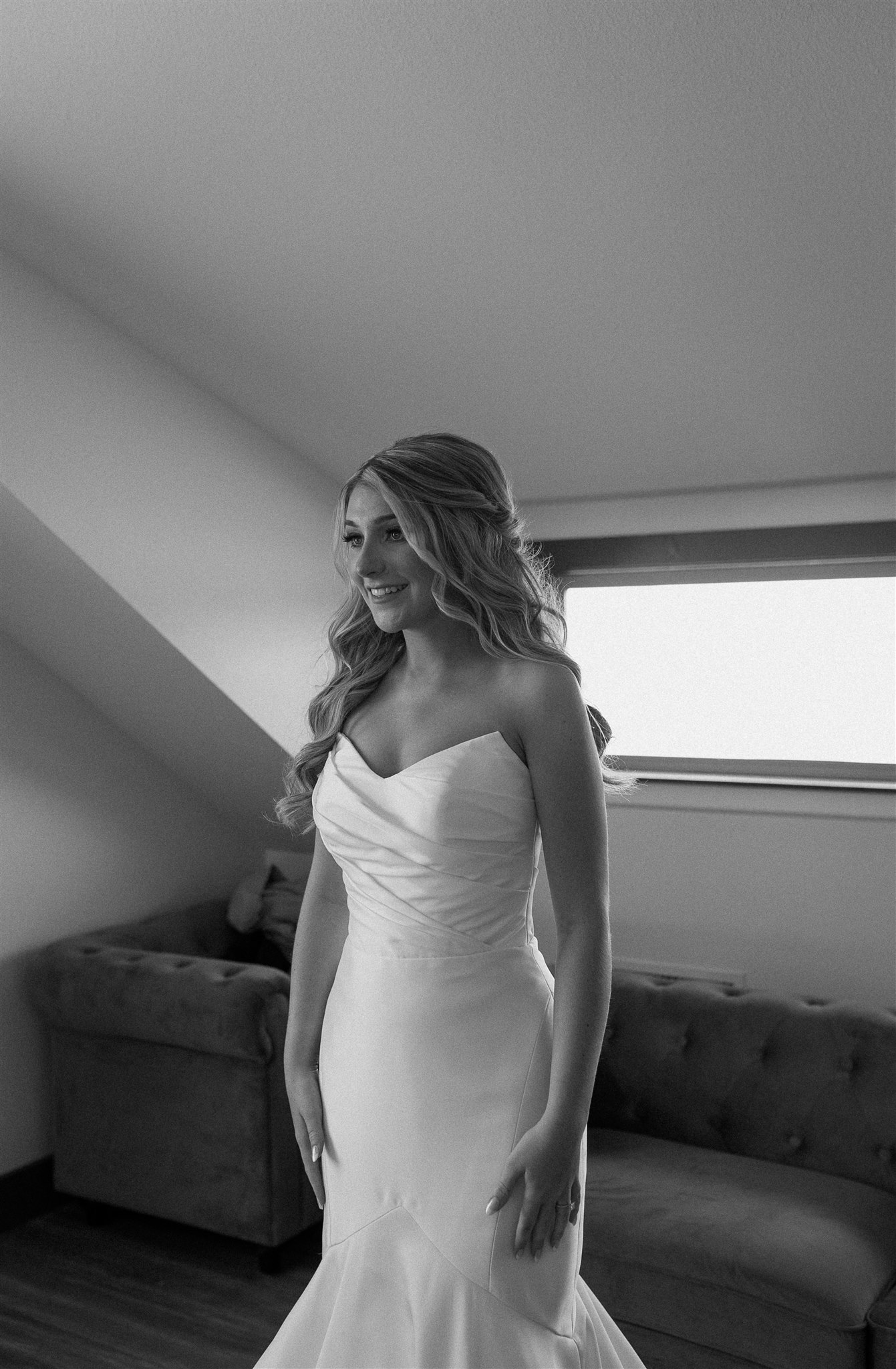 Black and white edit of bride standing in wedding attire looking into mirror.