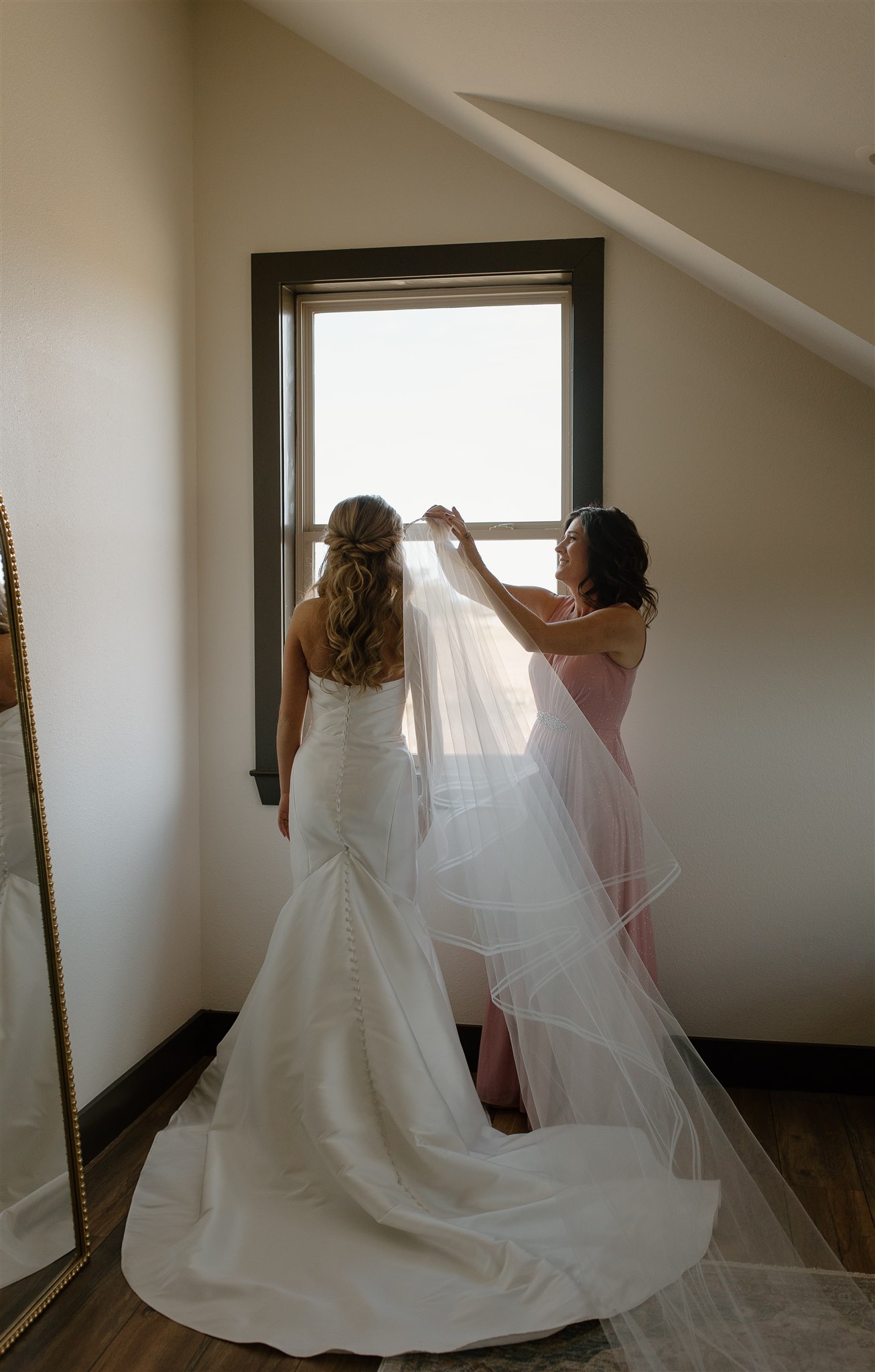 Mother of bride places veil into bride's wedding up-do.