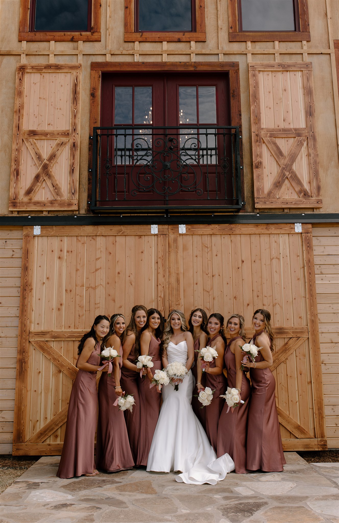 Bride and Bridesmaids pose in front of barn doors in wedding attire.