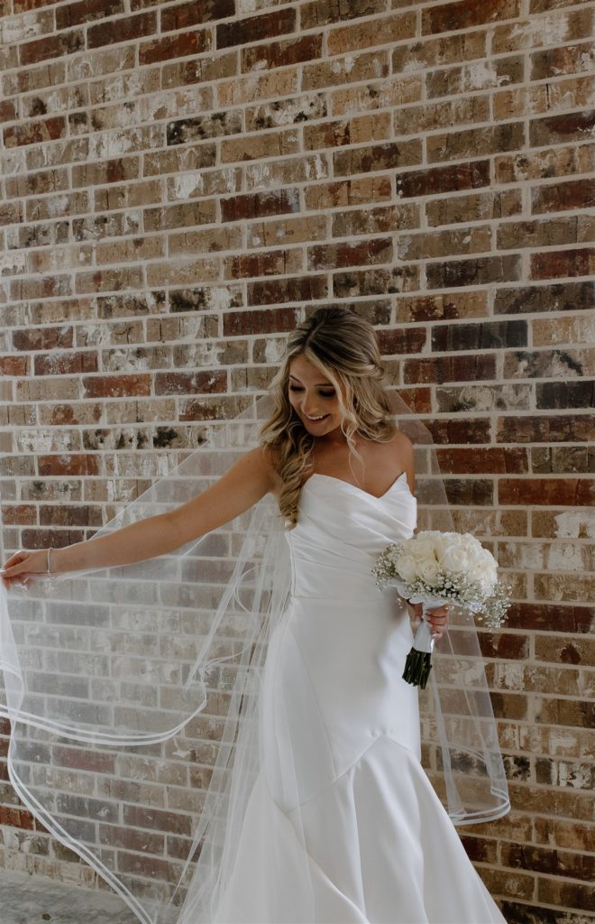 Bride plays with veil while holding her bouquet in wedding attire.