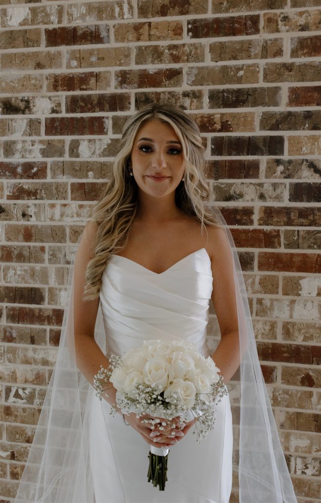 Bride soft smiles at camera while holding her white roses bouquet.