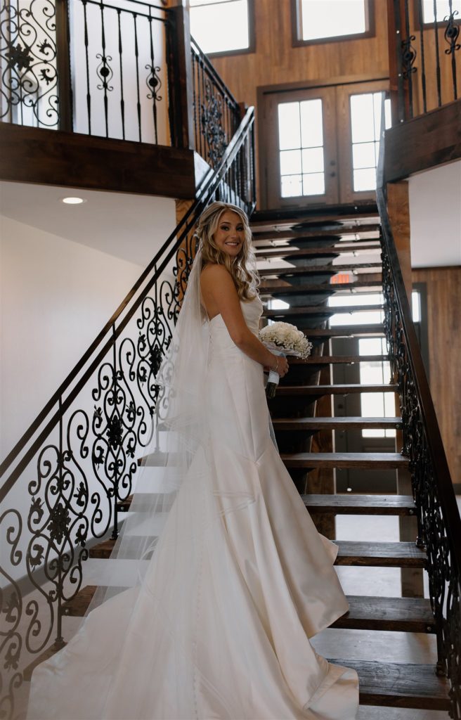 Bride stands on grand staircase at Texas wedding venue during bridal portraits.