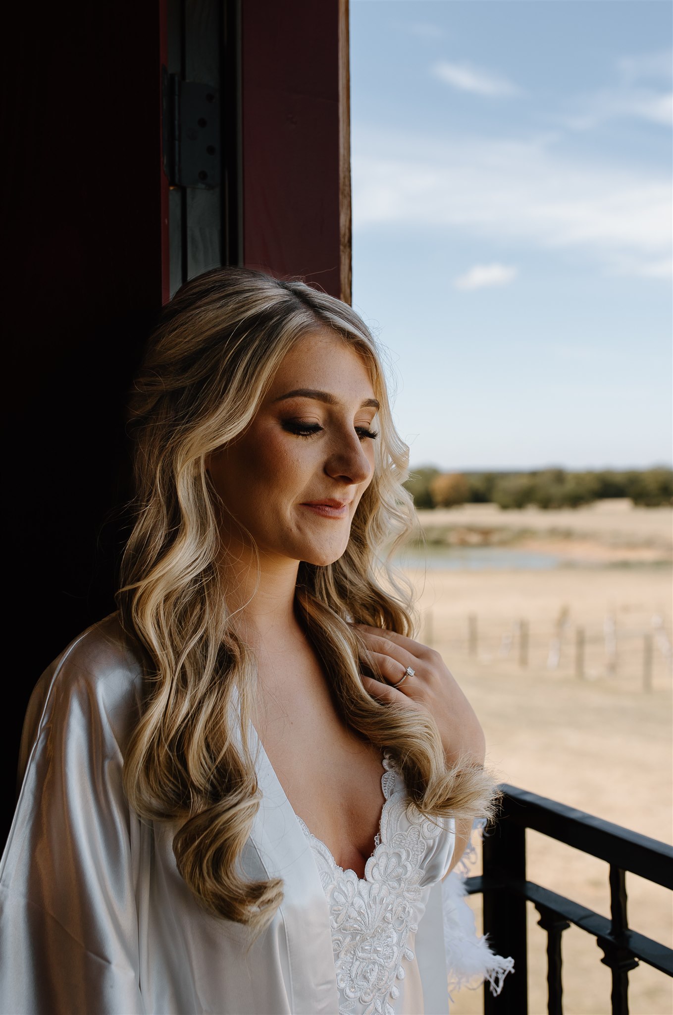 Bride stands at balcony overlooking Texas vineyard in wedding attire.