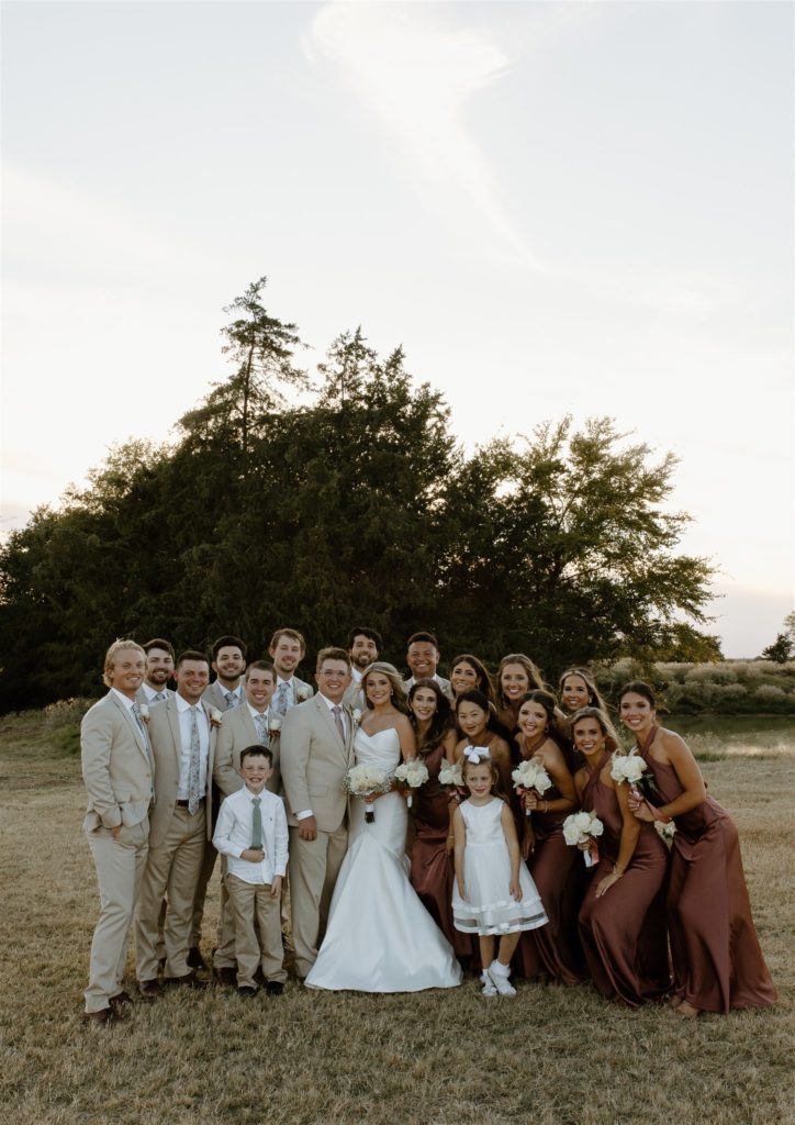 Wedding party groups together and smiles during texas outdoor wedding in the fall.