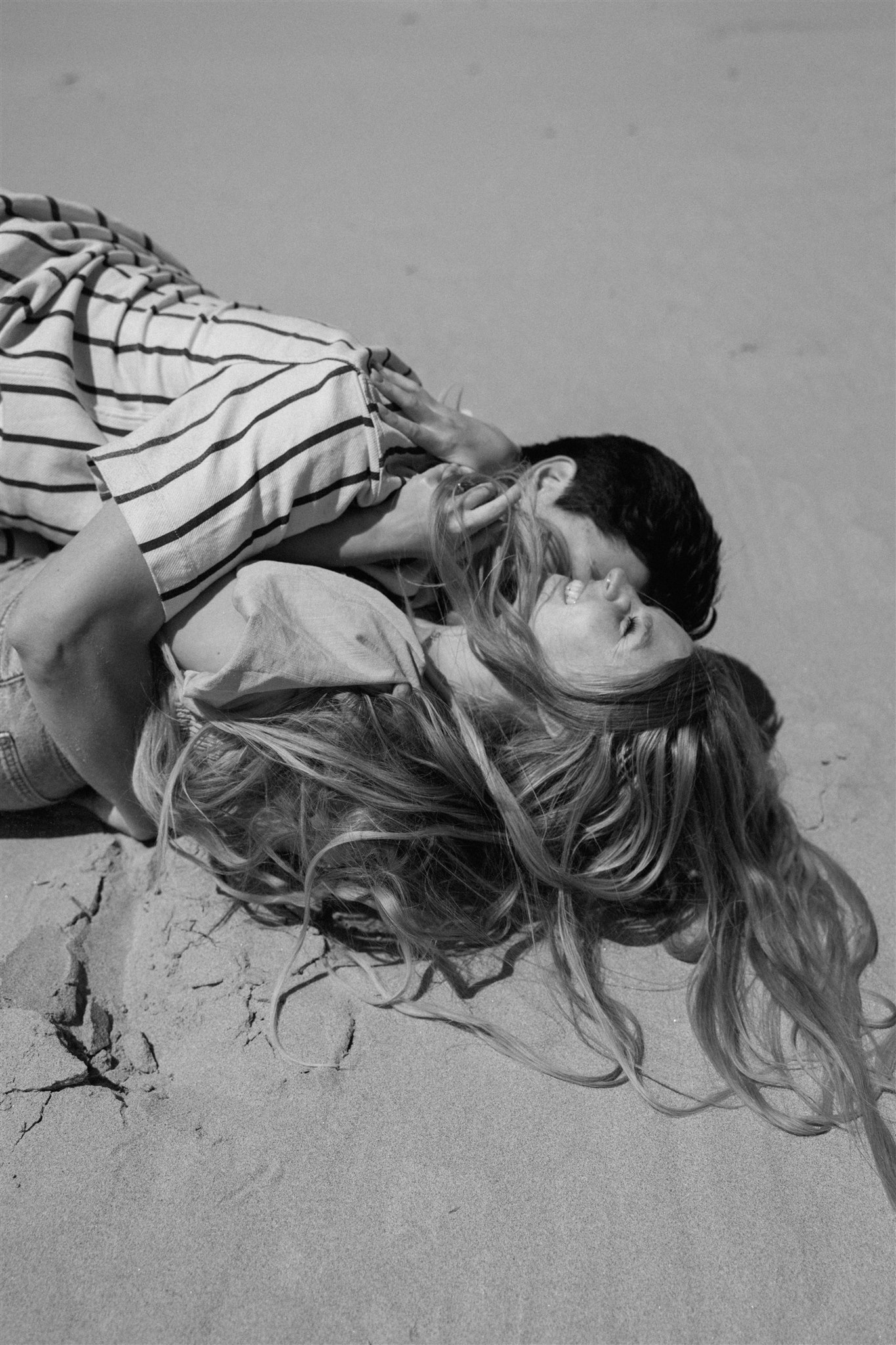 Engaged couple rolls in sand on Oregon Coast during engagement photos.